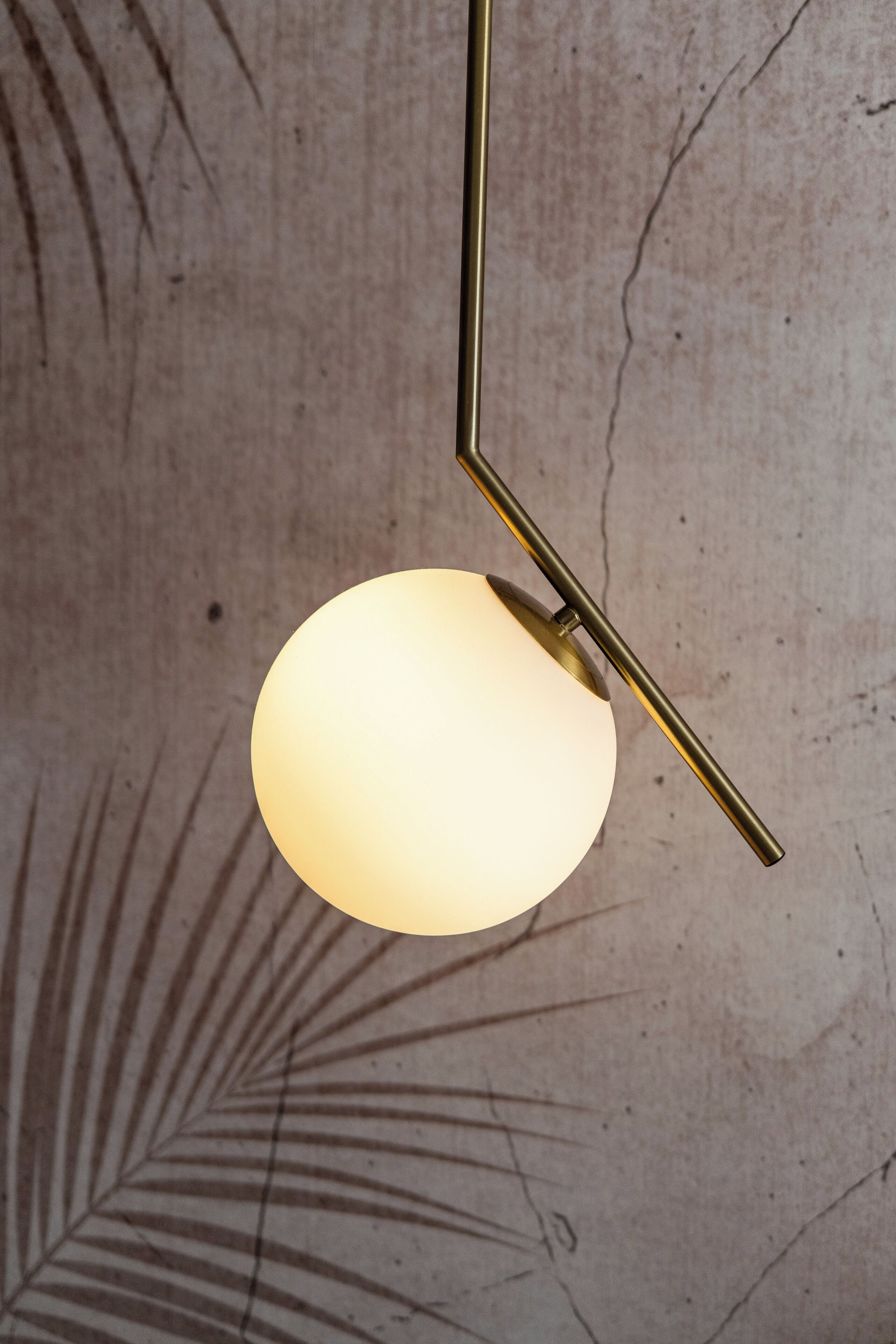 A pendant light fixture with a spherical shade and a metallic stand against a textured wall.