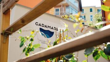 Letrero de 'CADAMARE' con logotipo y texto que indica 'HABITACIONES ENCANTADORAS EN PORTOVENERE'.