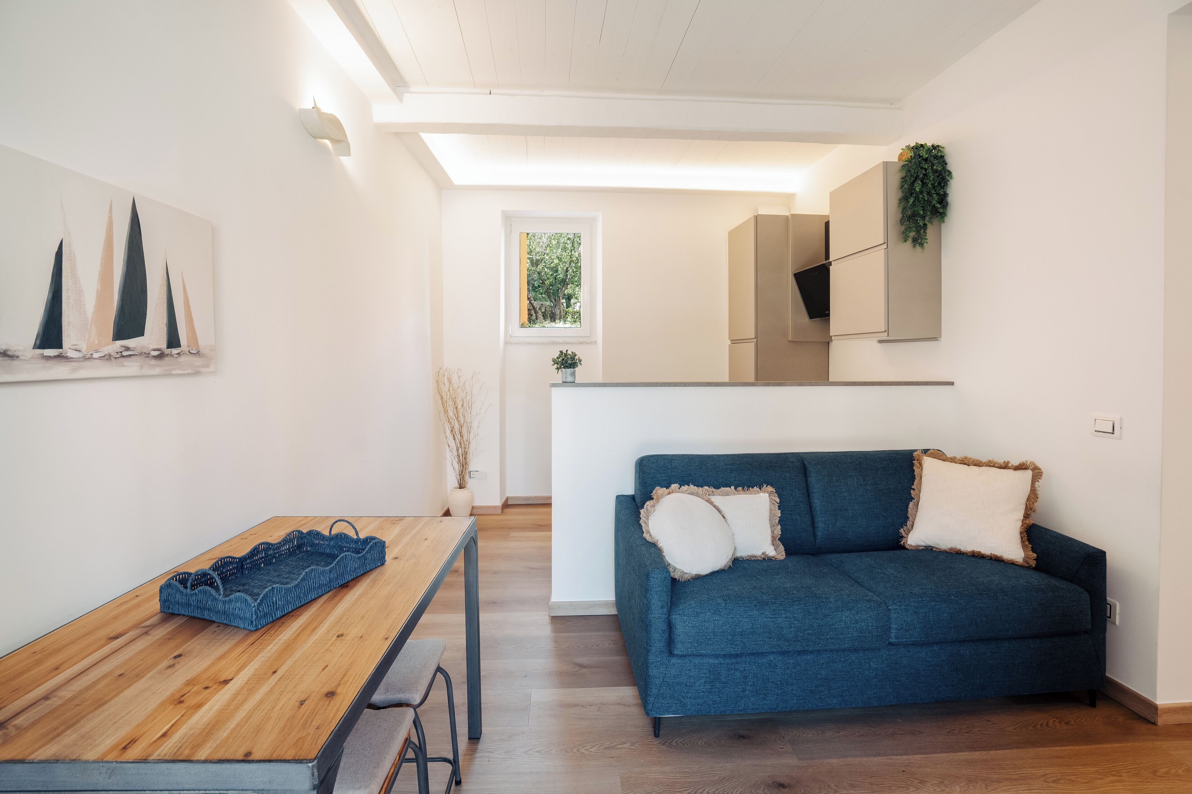 A modern living room with a wooden dining table, a blue sofa, and a kitchen area in the background.