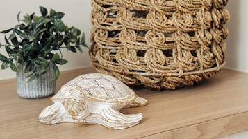 Una cesta tejida con asa, una planta pequeña en maceta y una figurita de tortuga sobre una superficie de madera.