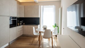 A modern kitchen with white cabinets, a black countertop, and a dining area with a round table and white chairs. - CADAMARE charming rooms in Portovenere (La Spezia)