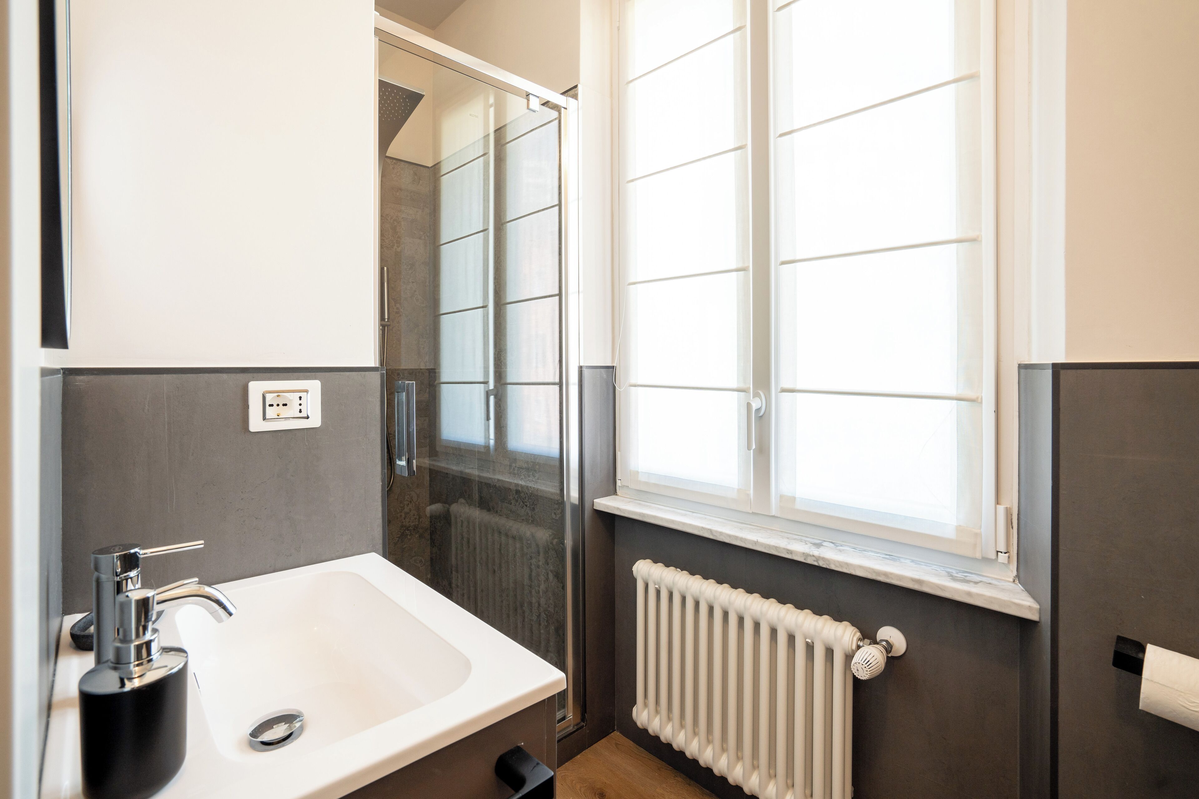 A modern bathroom with a white sink, a glass shower enclosure, and a window providing natural light.