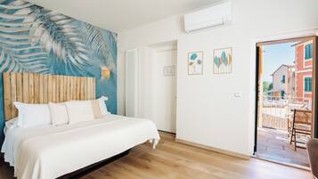 Ein Schlafzimmer mit einem Bett, einem Holzkopfbrett, einer blauen Wandmalerei, einem weißen Heizkörper und einer Tür, die zu einem Außenbereich mit Tisch und Stühlen führt.