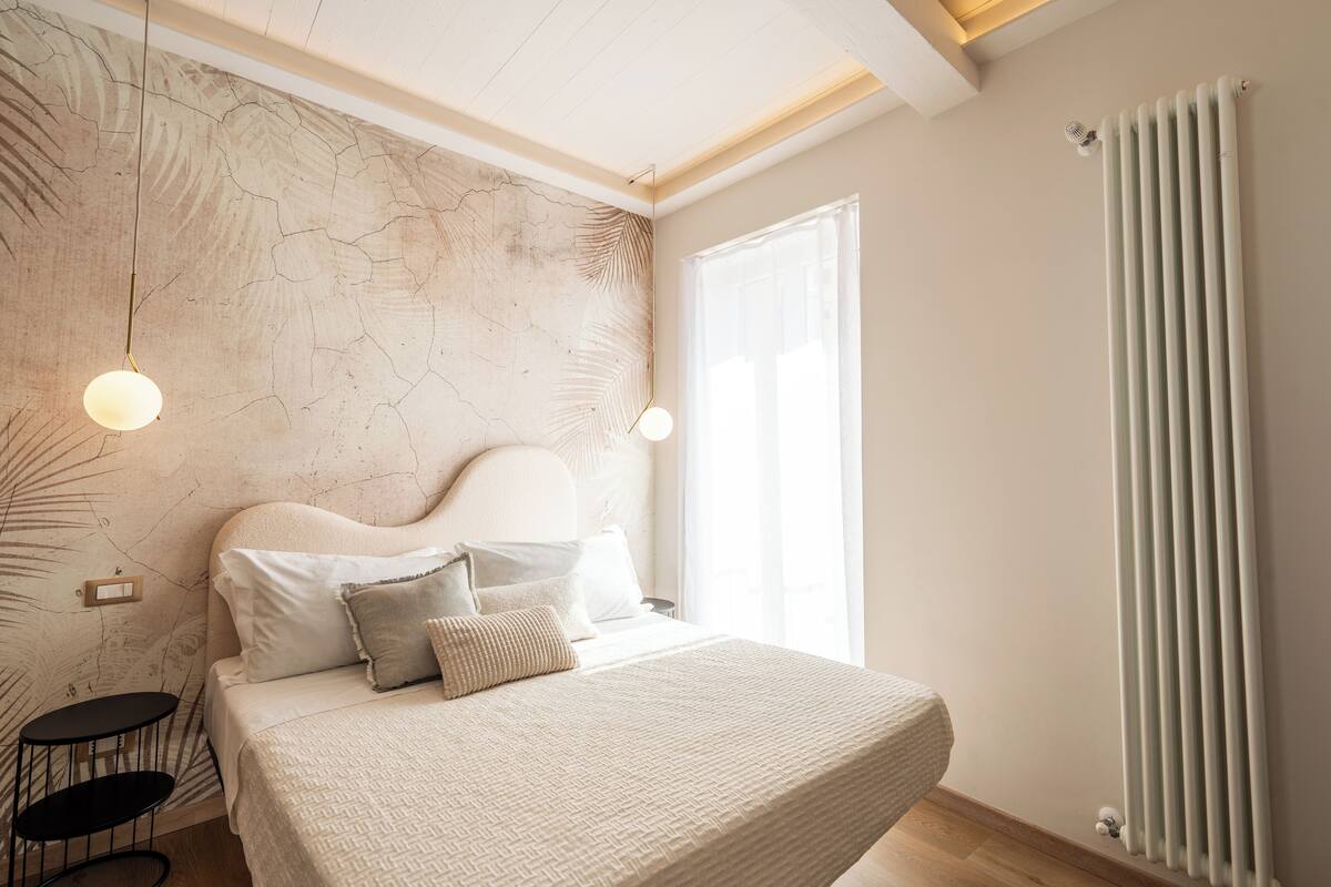 Een slaapkamer met een groot bed, een hoofdeinde, een nachtkastje, een wandlamp en een radiator.