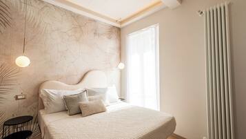 A bedroom with a large bed, a headboard, a nightstand, a wall-mounted light, and a radiator.