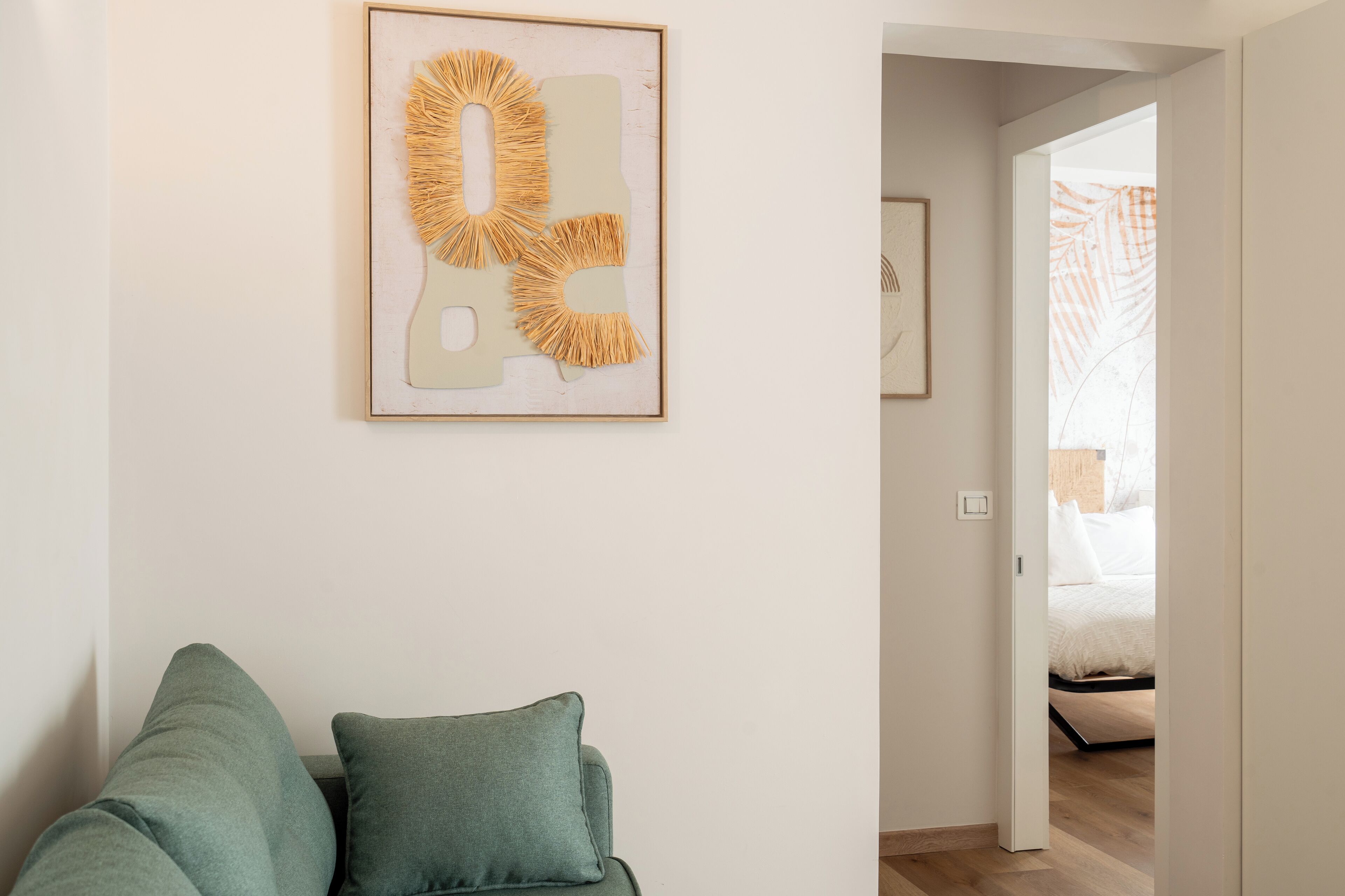 Una sala de estar moderna con un sofá, una obra de arte abstracta enmarcada y un acceso a un dormitorio.