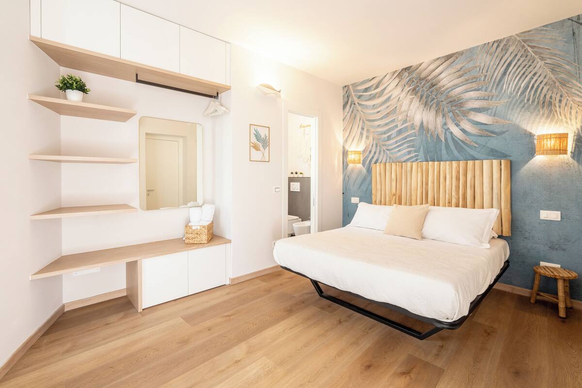 Een slaapkamer met een bed, houten planken, een spiegel, een wandlamp en een deur.