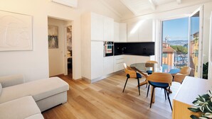 A modern living room with a sofa, a dining table with chairs, and a kitchen area with cabinets and a TV. - CADAMARE charming rooms in Portovenere (La Spezia)