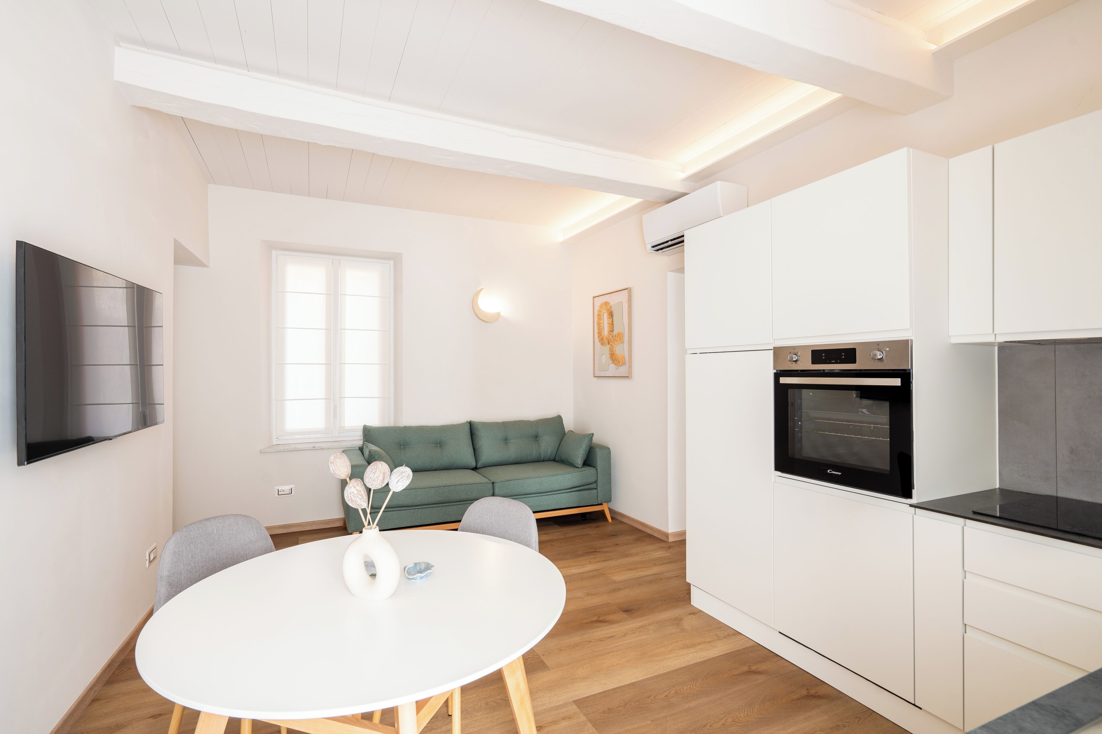 A modern kitchen with white cabinets, a built-in oven, and a dining area with a round table and chairs.