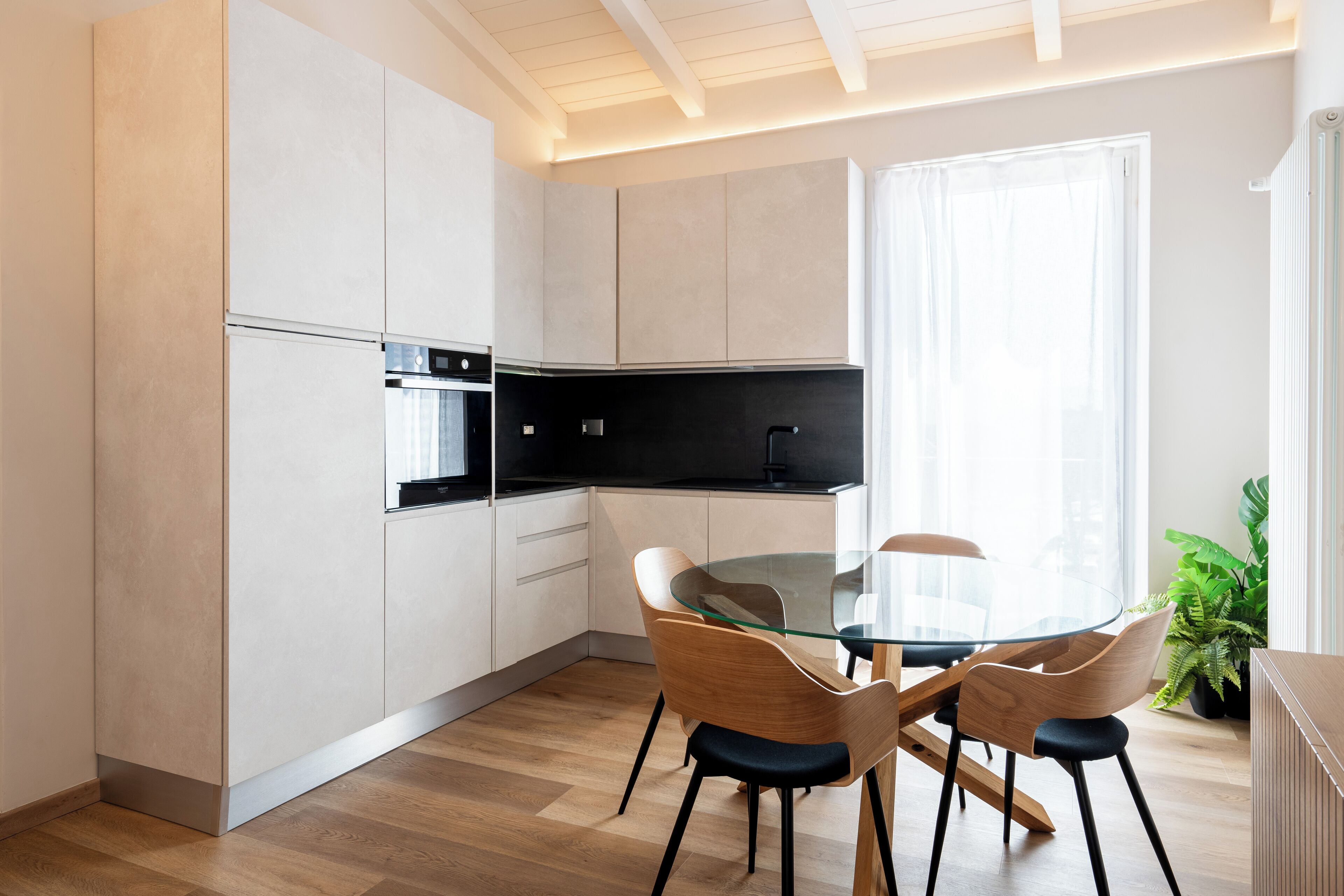 Una cocina moderna con armarios blancos, encimera negra y mesa de comedor de vidrio con sillas de madera.