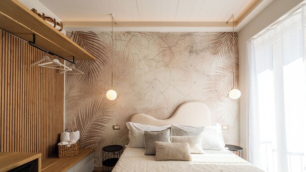 A modern bedroom with a wooden headboard, a large bed with multiple pillows, a hanging light fixture, and a shelf with towels. - CADAMARE charming rooms in Portovenere (La Spezia)