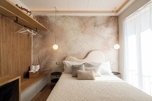 A modern bedroom with a wooden headboard, a large bed with multiple pillows, a hanging light fixture, and a shelf with towels. - CADAMARE charming rooms in Portovenere (La Spezia)