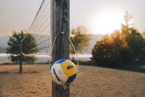A volleyball hanging on a net, with a blurred background of trees and a body of water.