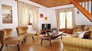 Ein gemütliches Wohnzimmer mit einer Couch, zwei Sesseln, einem Holztisch, einem Fernseher und einer Treppe.
