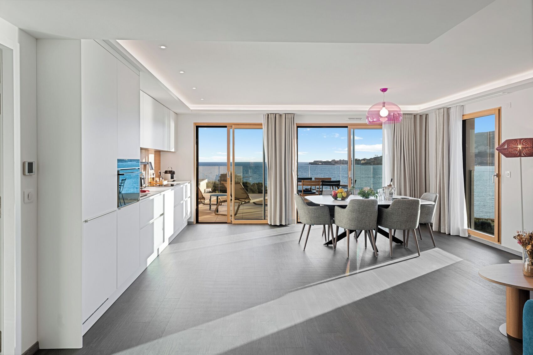 Habitación de hotel moderna con comedor, cocina y balcón con vistas al mar.