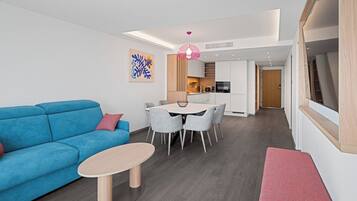 A modern living room with a blue sofa, a round coffee table, and a dining area with grey chairs.