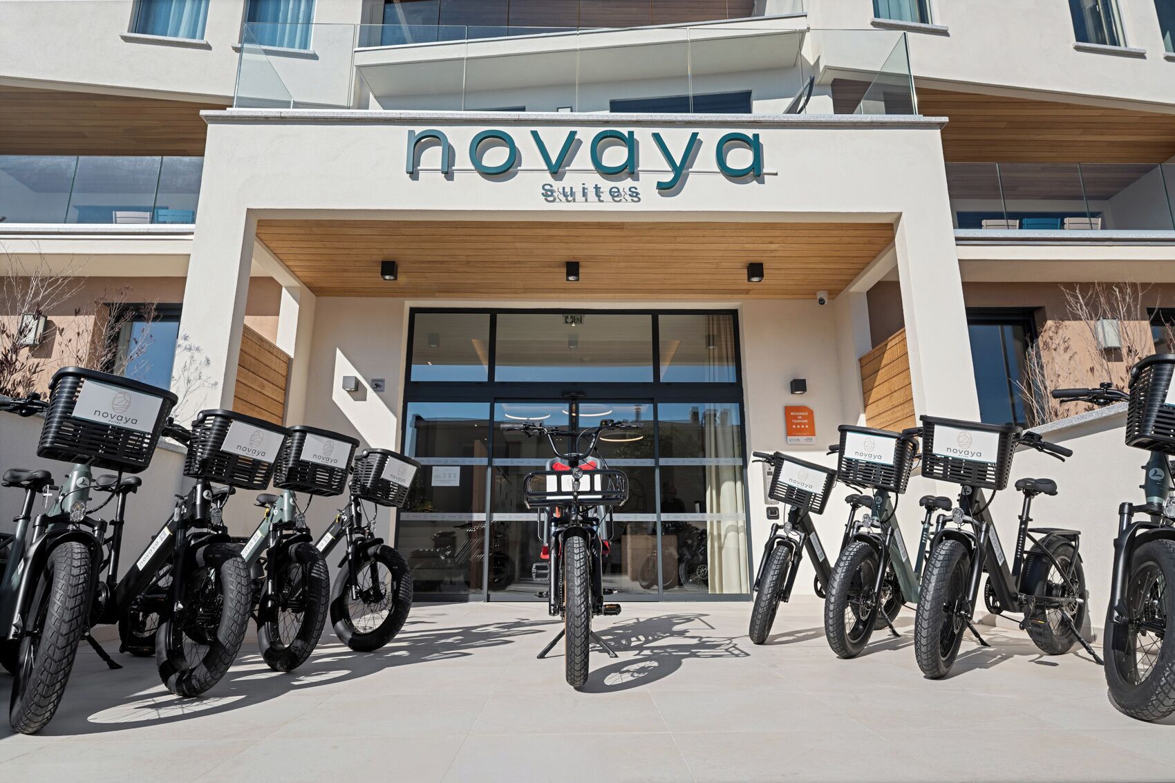 A modern building with a sign reading 'novaya Suites' and several bicycles parked in front.