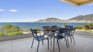 A terrace with a table set for dining, overlooking a coastal cityscape with mountains in the background.