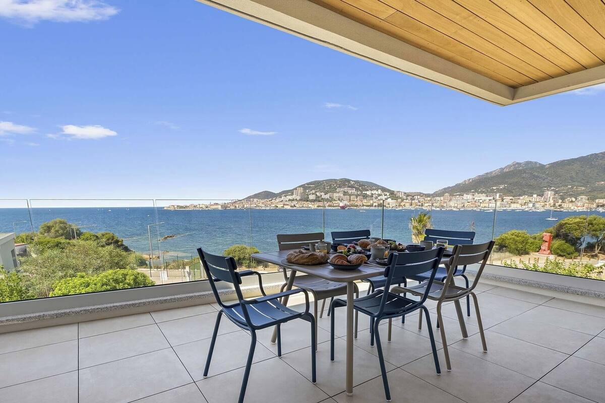 A terrace with a table set for dining, overlooking a coastal cityscape with mountains in the background.
