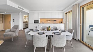 A modern dining area with a round table, grey upholstered chairs, and a kitchen in the background.