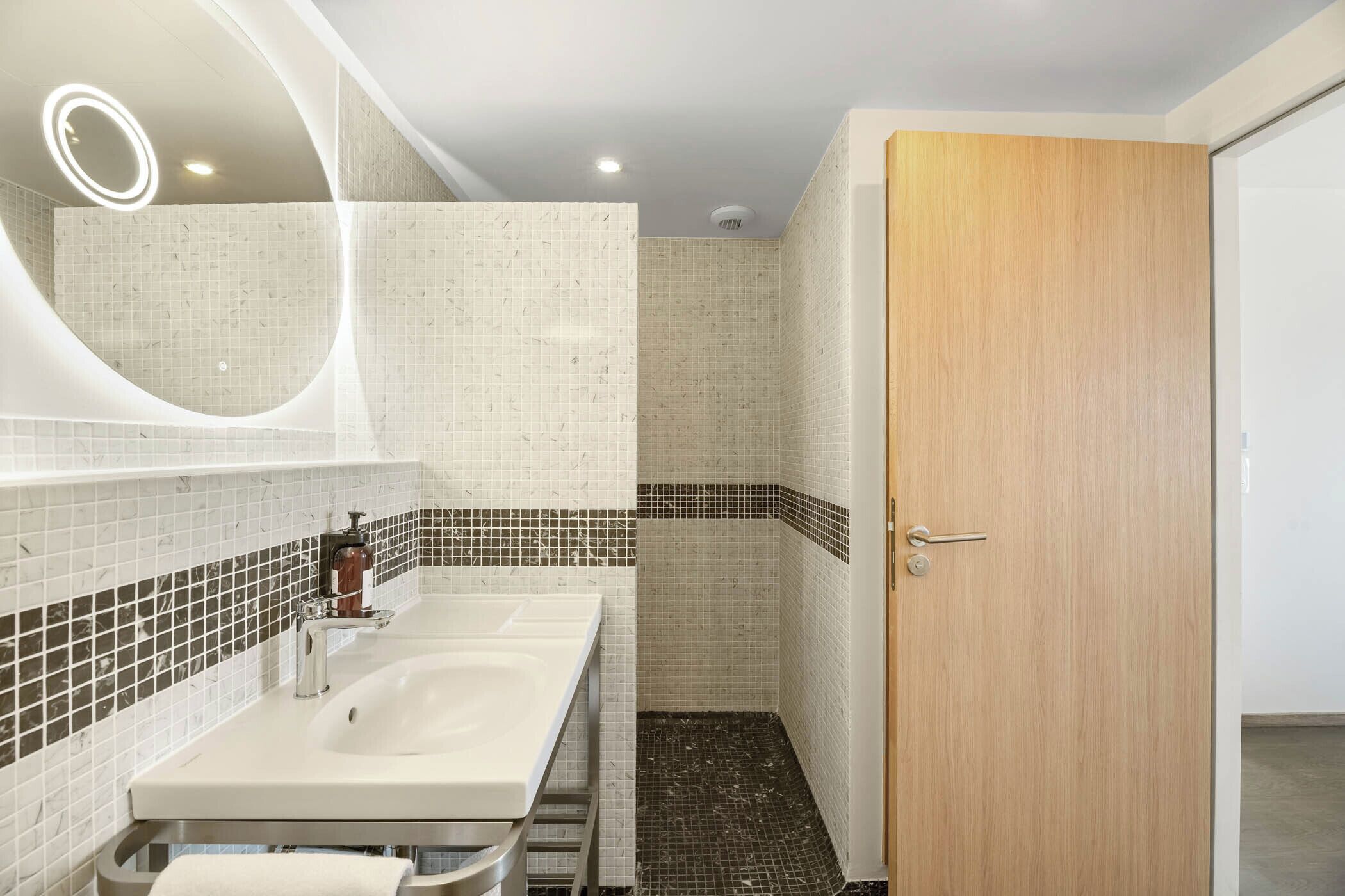 A modern bathroom with two sinks, a mirror, and a shower area.