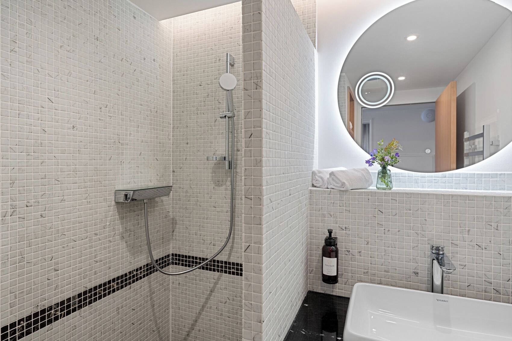 Ein modernes Badezimmer mit Dusche, Badewanne und einem Spiegel mit runder Beleuchtung.