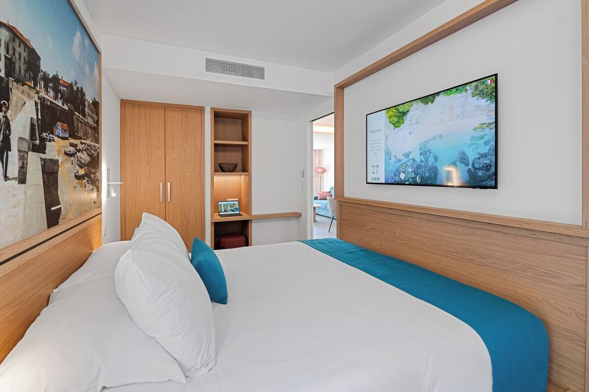 A hotel room with a large bed, a wooden wardrobe, a television mounted on the wall, and a painting on the wall.