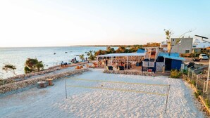 A beach volleyball court with a net, stone walls, and a few tables. - Zanzibar FumbaTown B08-02-12 (Fumba)