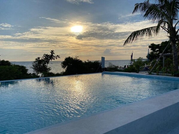 A swimming pool with a sunset view, surrounded by greenery and palm trees.