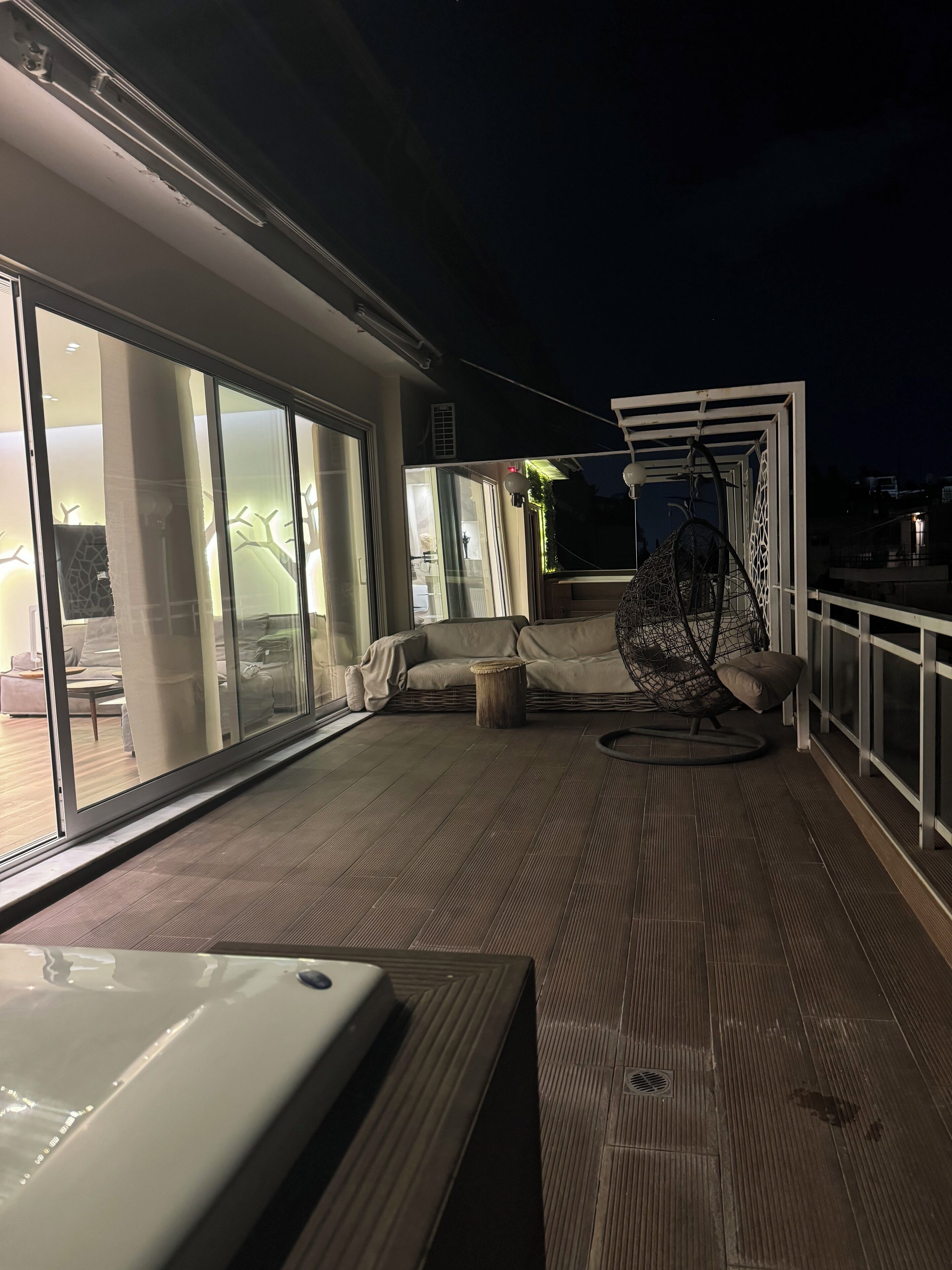 A deck with a swing chair, a cushioned seating area, and a view of the outside.