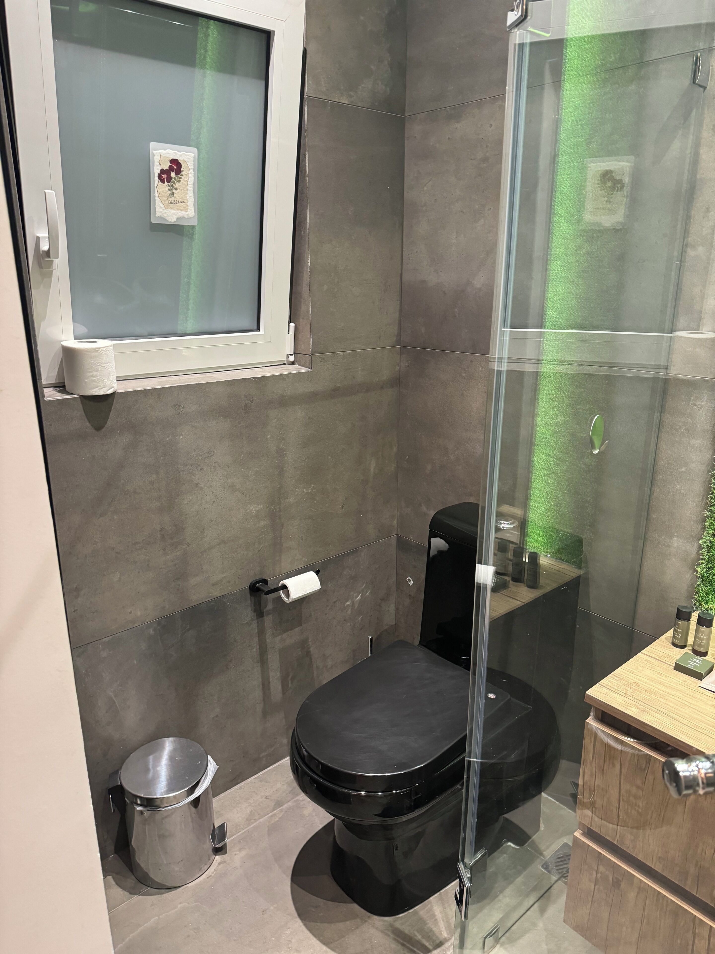 A modern bathroom with a glass-enclosed shower, a toilet, and a small trash bin.