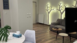Una sala de estar moderna con piso de madera, un sofá gris, una mesa redonda con un mantel tejido y una decoración de árbol montada en la pared.