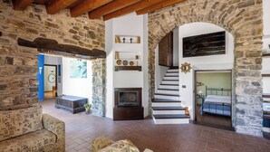A spacious living area with a stone fireplace, a sofa, and a staircase leading to a bedroom. - Villa Granci con Piscina by Wonderful Italy (Polizzi Generosa)