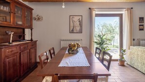 A dining area with a wooden table, chairs, a cabinet with glass doors, a radiator, a framed picture on the wall, and a view of the outdoors through a door. - Villa Granci con Piscina by Wonderful Italy (Polizzi Generosa)