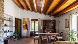 A rustic interior with exposed wooden beams, a dining area with a table and chairs, a stone wall with shelves, and a large window with curtains. - Villa Granci con Piscina by Wonderful Italy (Polizzi Generosa)