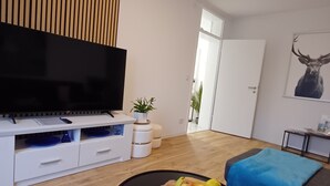 A modern living room with a flat-screen TV, a round coffee table with apples, a sofa, and a blue throw blanket. - Apartment Busch in the center (Bad Harzburg)
