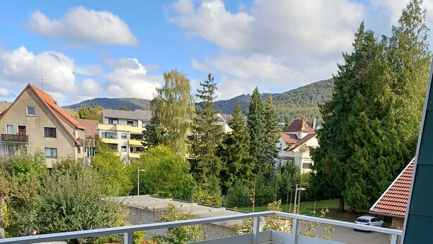 A balcony with two cushioned chairs and a small table, overlooking a residential area with houses and trees. - Apartment Busch in the center (Bad Harzburg)