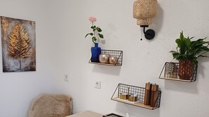 A dining area with a white table, four white chairs, a woven wall lamp, and two wall-mounted shelves with decorative items. - Apartment Busch in the center (Bad Harzburg)