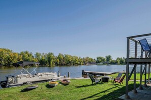A lakeside dock with boats, a covered seating area, and a grassy lawn.