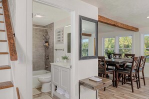 A bathroom with a shower, toilet, and vanity. There is a dining area with a table and chairs.