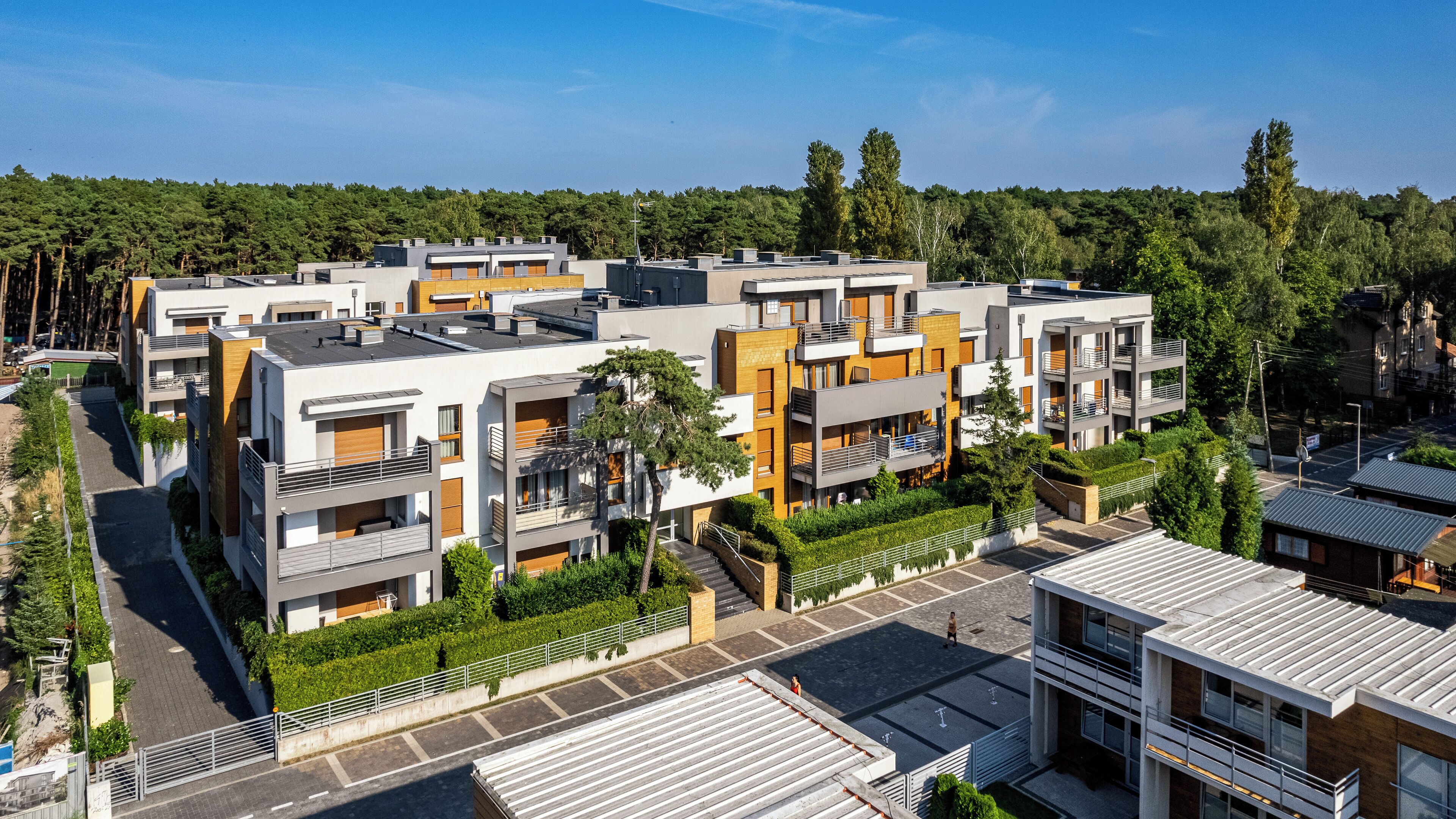 Un edificio residencial moderno con varios balcones, un patio central y una zona verde circundante.