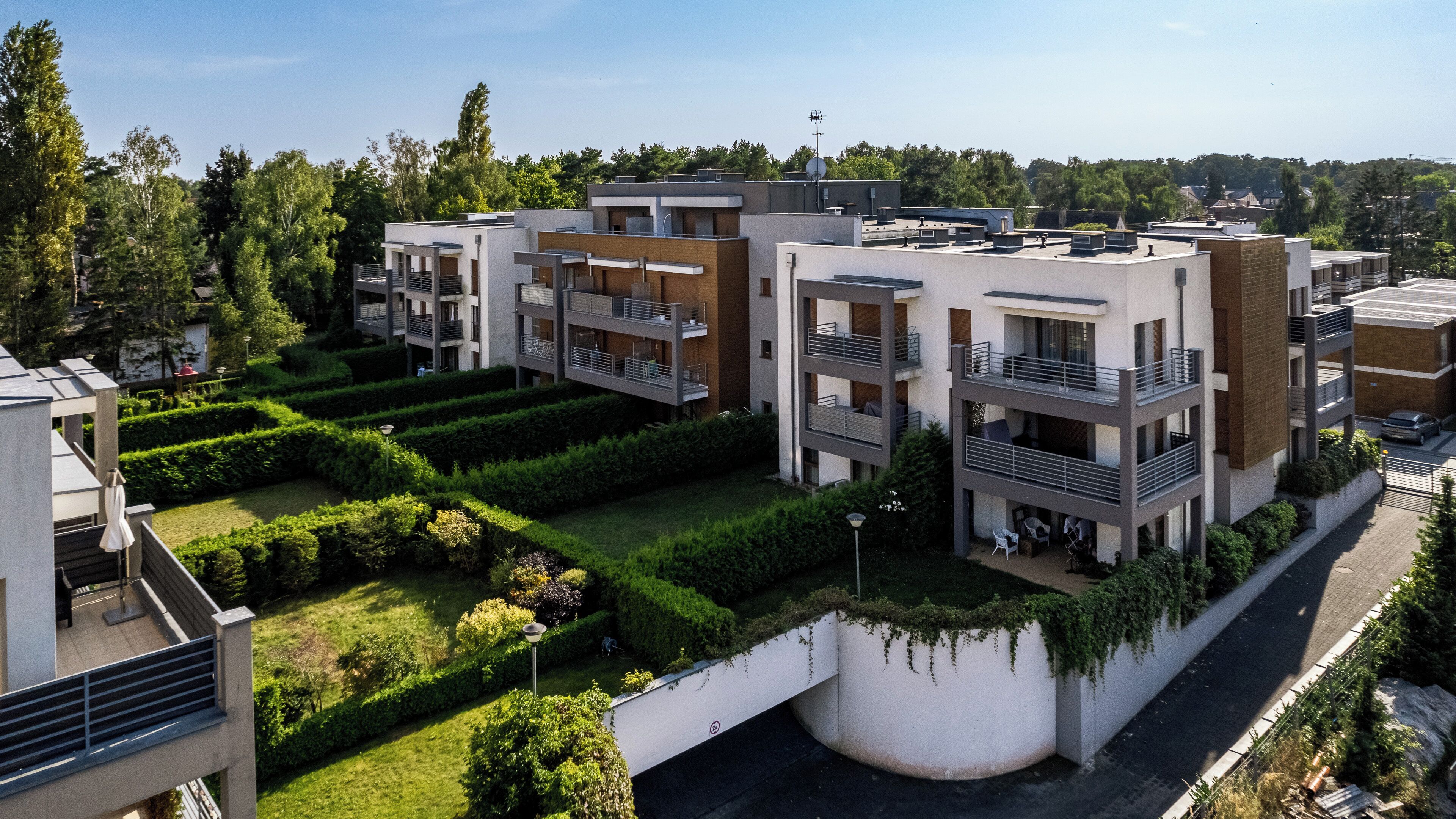 A modern multi-story residential building with balconies, a landscaped garden, and a clear view of the surrounding area.