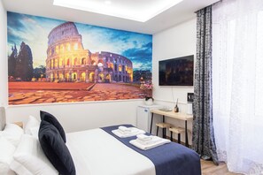 A hotel room with a large painting of the Colosseum, a bed with white linens, a desk with a computer, and a small refrigerator. - Susy's Guest House (Rome)
