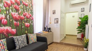 Un área de recepción moderna con un sofá, almohadones coloridos, una estación de café y un gran mural floral.