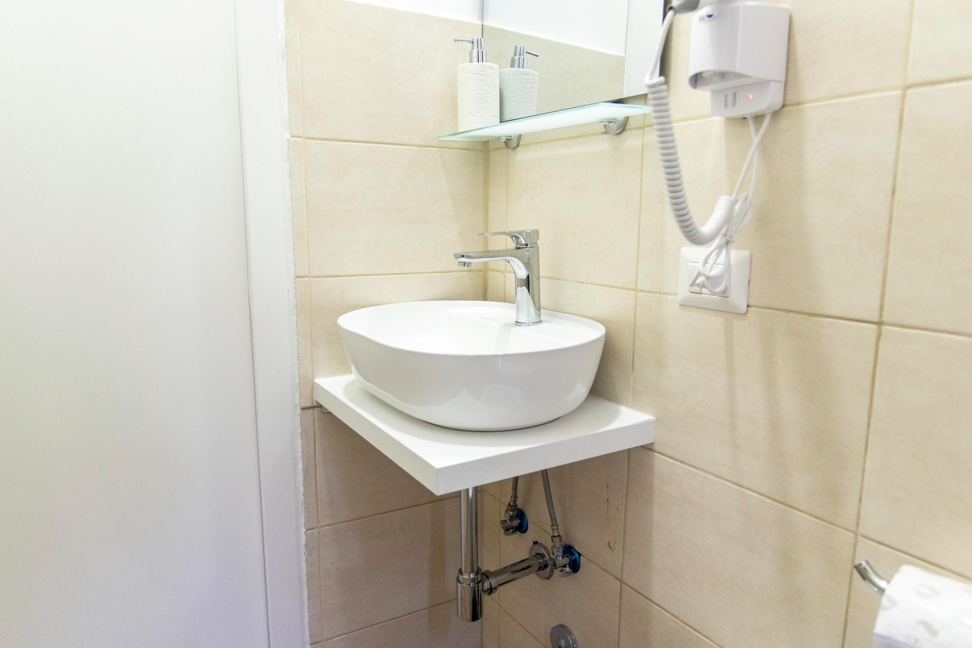 A bathroom with a white sink, a mirror, and a towel dispenser.