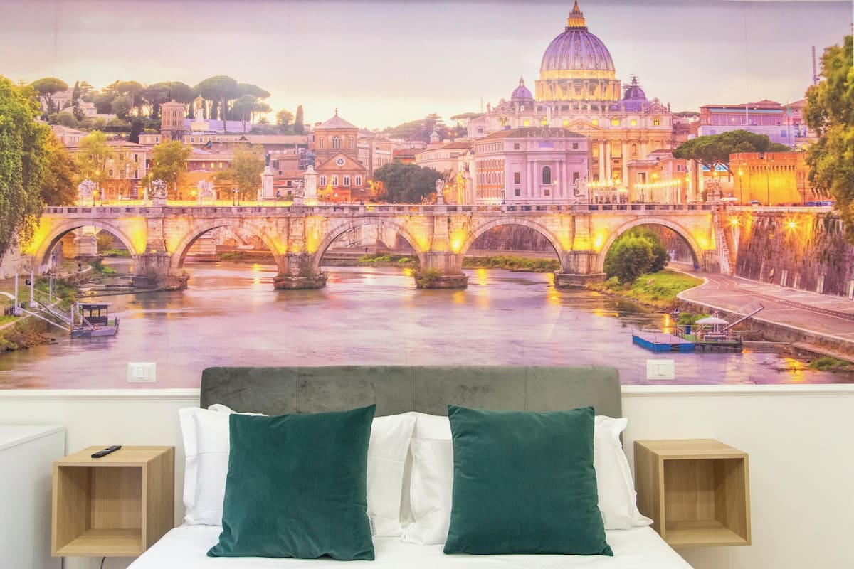 A bedroom with a mural of a cityscape, a bed with green and white pillows, and two bedside tables.