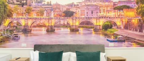 Quarto com um mural de paisagem urbana, uma cama com almofadas verdes e brancas, e duas mesinhas de cabeceira.