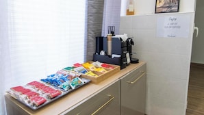 Una barra de desayuno con diversos bocadillos, una máquina de café y un cartel que ofrece té o café.