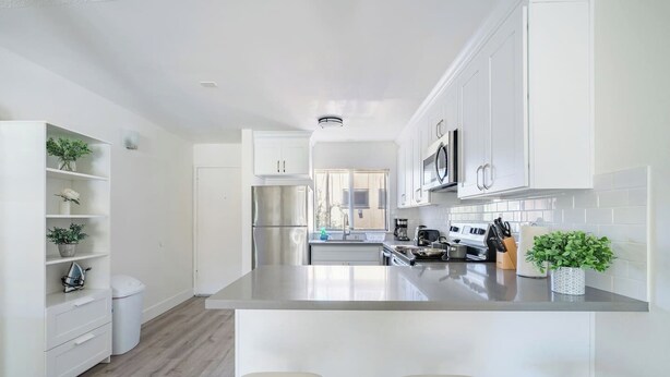Una cocina moderna con armarios blancos, electrodomésticos de acero inoxidable y una isla central con taburetes de bar.
