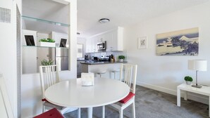 Cocina moderna con armarios blancos, una isla central y una zona de comedor con una mesa redonda y sillas.